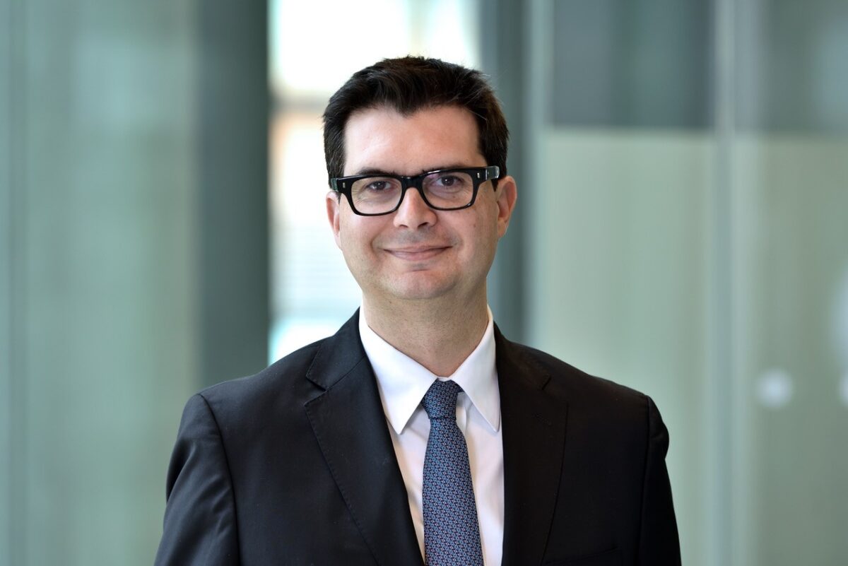 Otávio Berwanger, cardiologista brasileiro, usando terno e gravata em ambiente corporativo, com fundo de vidro desfocado