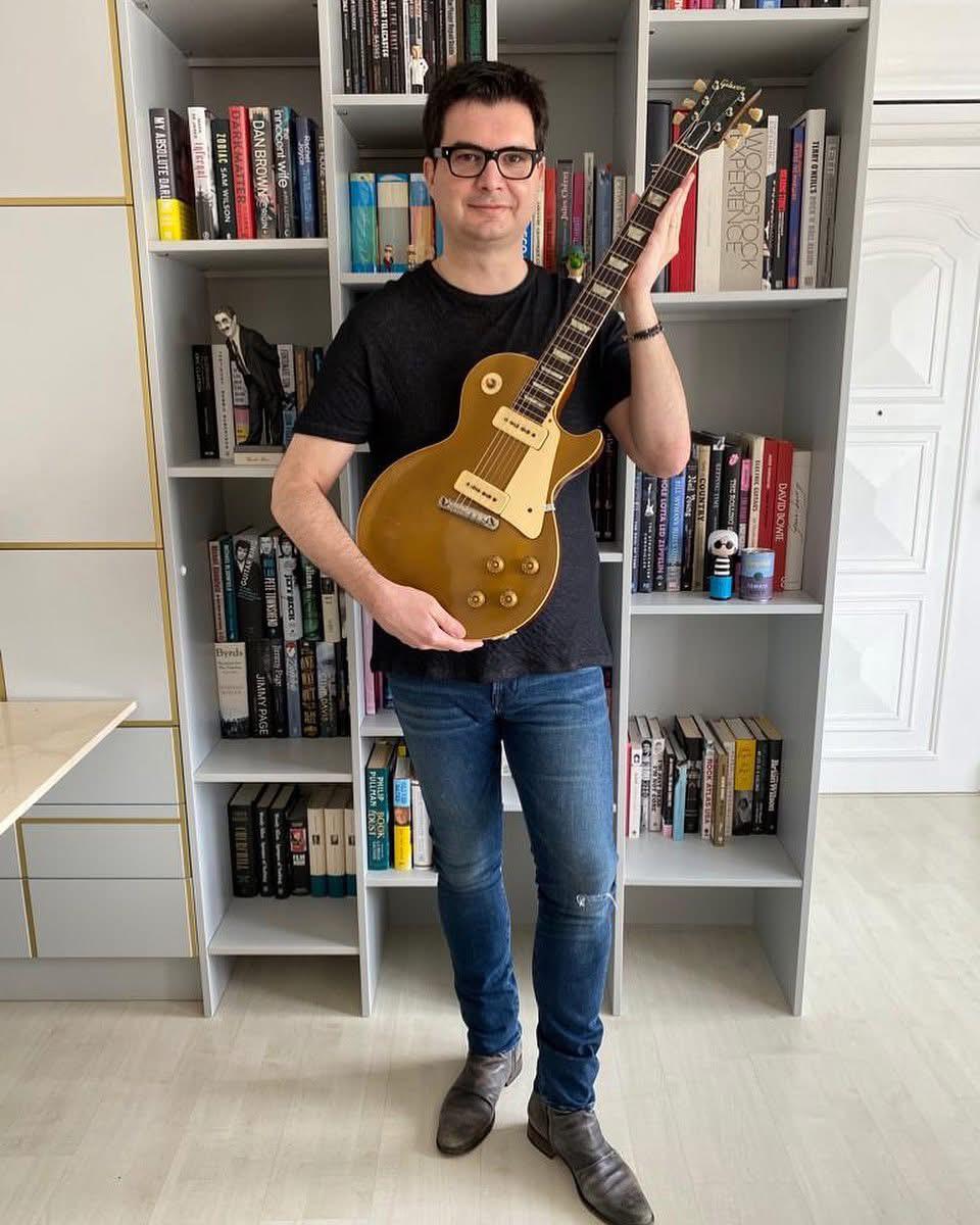 Otávio Berwanger, cardiologist and executive director of the George Institute for Global Health, holding a vintage Les Paul guitar in his home, with a bookshelf in the background