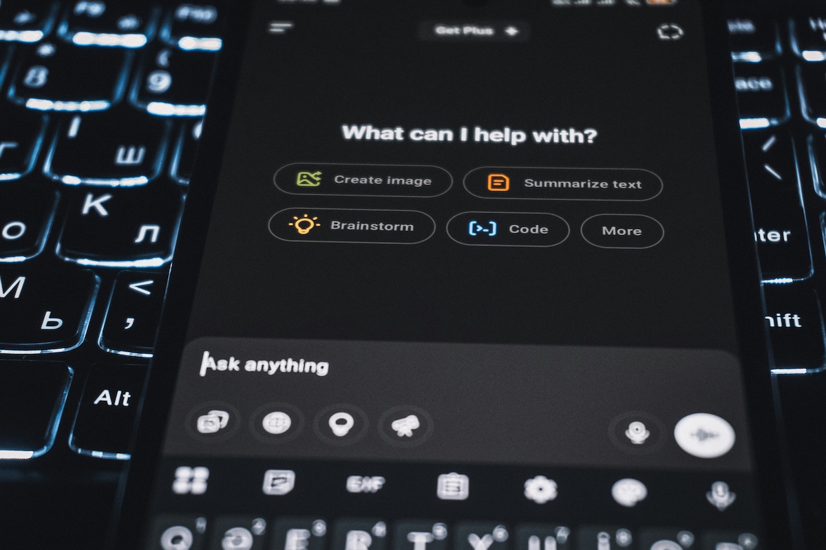 Tela de um celular exibindo a interface de um aplicativo de inteligência artificial generativa, com as opções "Create image", "Summarize text", "Brainstorm", "Code" e "More", sobre um teclado retroiluminado.