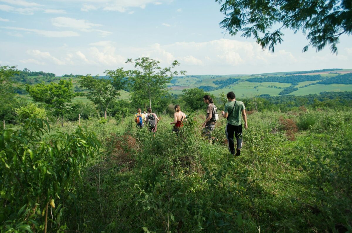 The image shows a group of people walking in the natural environment, with a landscape of mountains and low-level vegetation