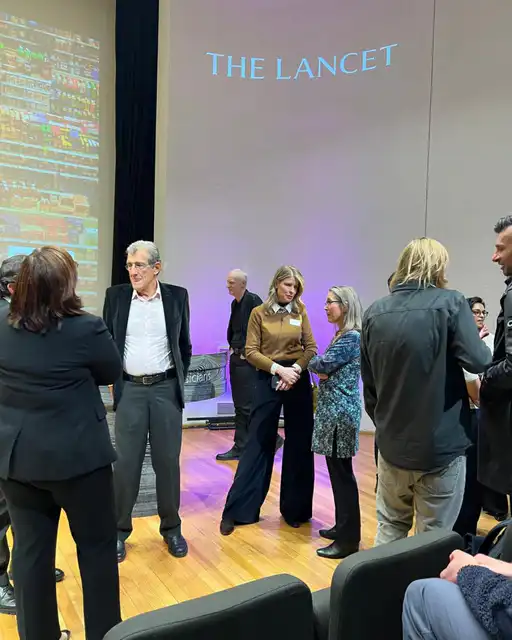 People chatting informally in an auditorium at a scientific event, with images from the Lancet projected in the background.