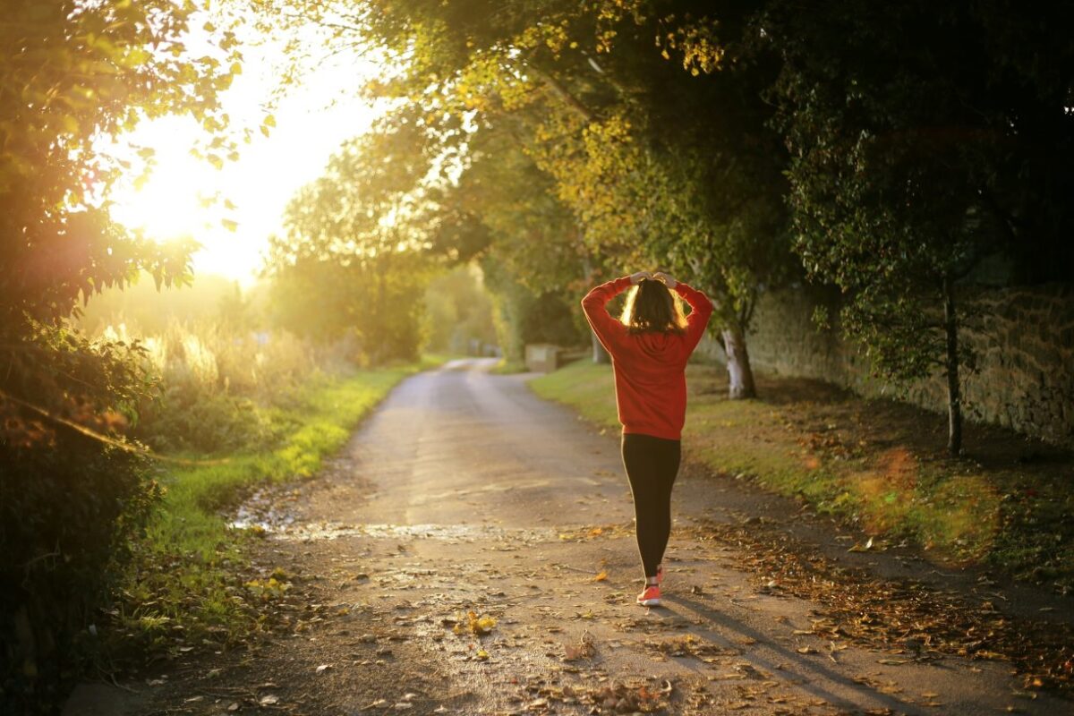 A person walking along a tree-lined road at dusk, illuminated by the golden light of the setting sun. The image conveys a sense of tranquility, movement, and connection with nature.