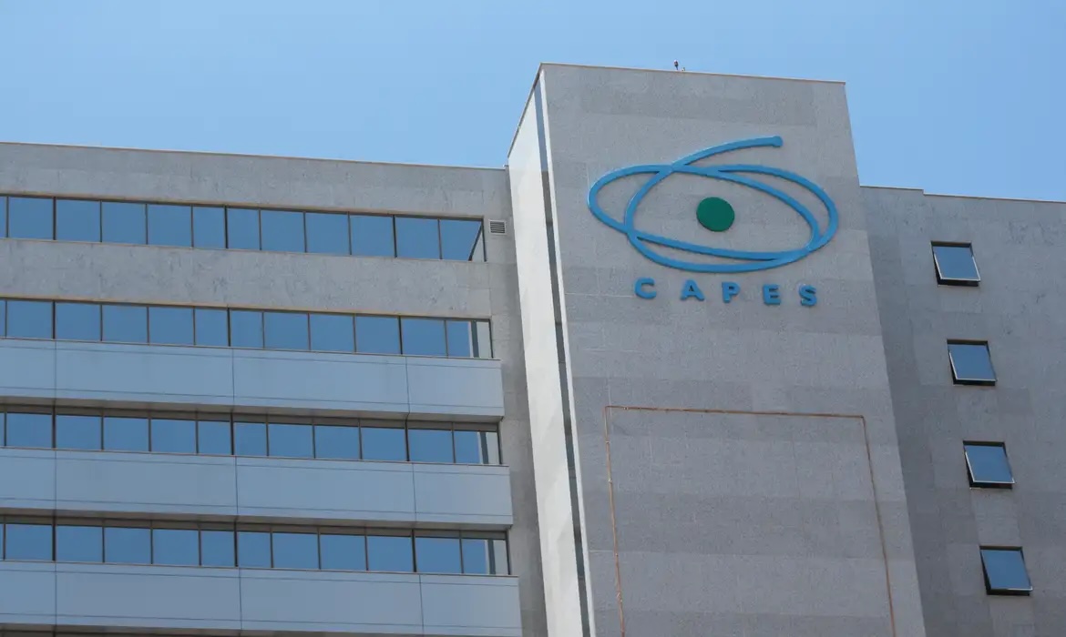 Fachada do edifício-sede da CAPES em Brasília, com logotipo azul da instituição em destaque sobre parede de concreto, ao fundo céu azul claro