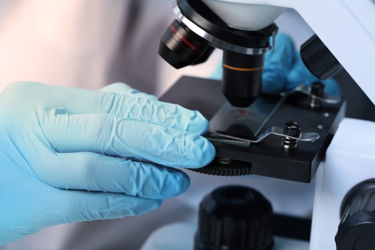 Pesquisadora analisa amostras em laboratório durante procedimento de investigação científica com microscópio. A imagem remete a pesquisa biomédica, inovação e análise laboratorial
