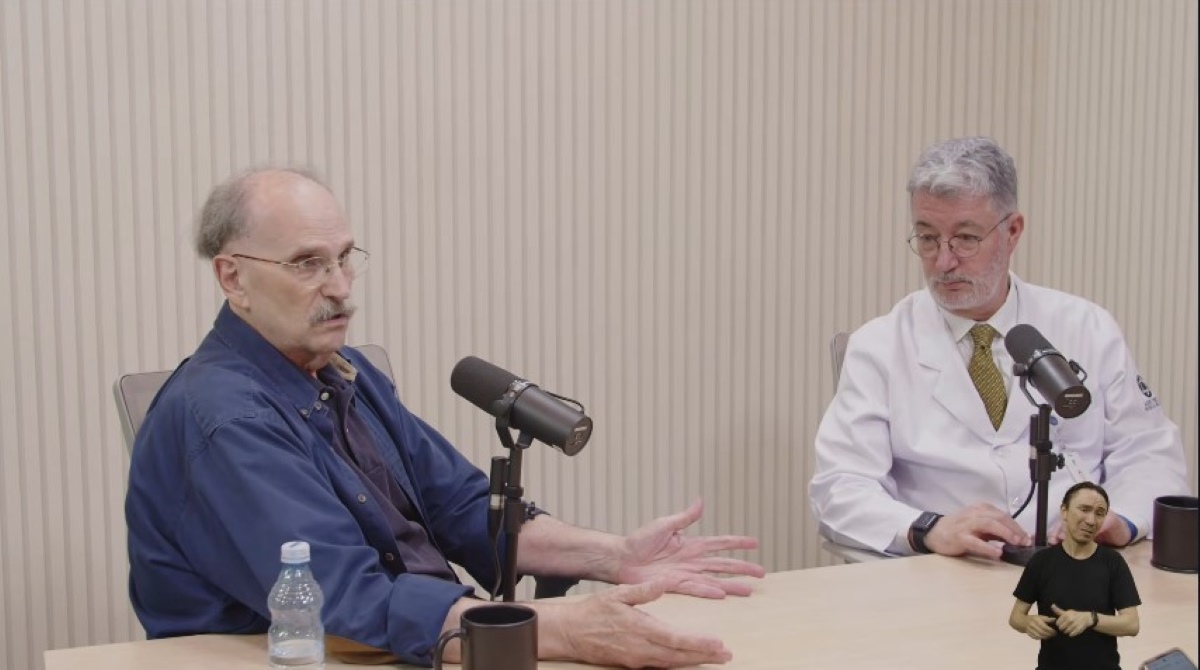 Two participants, Glauco Arbix and Luiz Vicente Rizzo, are speaking in a studio with microphones on the table and sign language interpretation in the corner of the screen