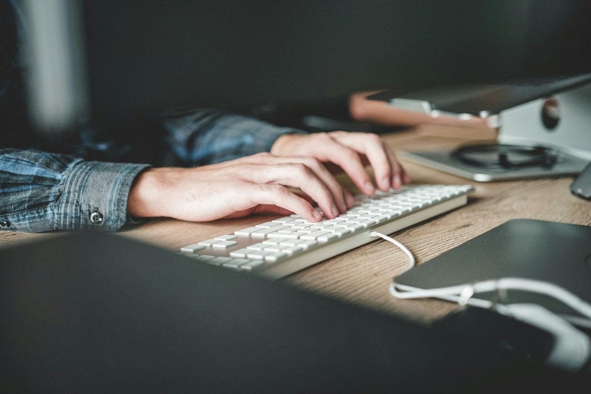 Hands typing on a keyboard on an office desk, in a setting with soft lighting and selective focus. The image suggests writing, editing, or digital content production.