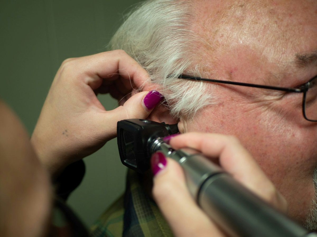 A healthcare professional uses an otoscope to examine the ear of an elderly patient. The image shows a routine clinical procedure for assessing hearing.