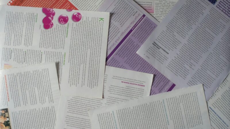 The image shows an overhead view of printed scientific pages overlapping eachother haphazardly on a flat surface. In the center, a text box on one page is highlighted in purple.